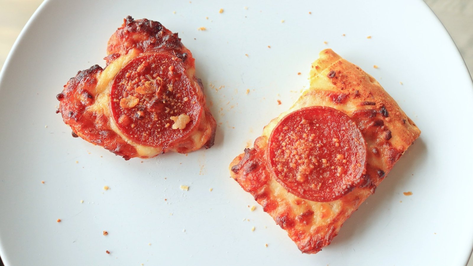 A small heart-shaped pepperoni pizza and a small rectangular slice.