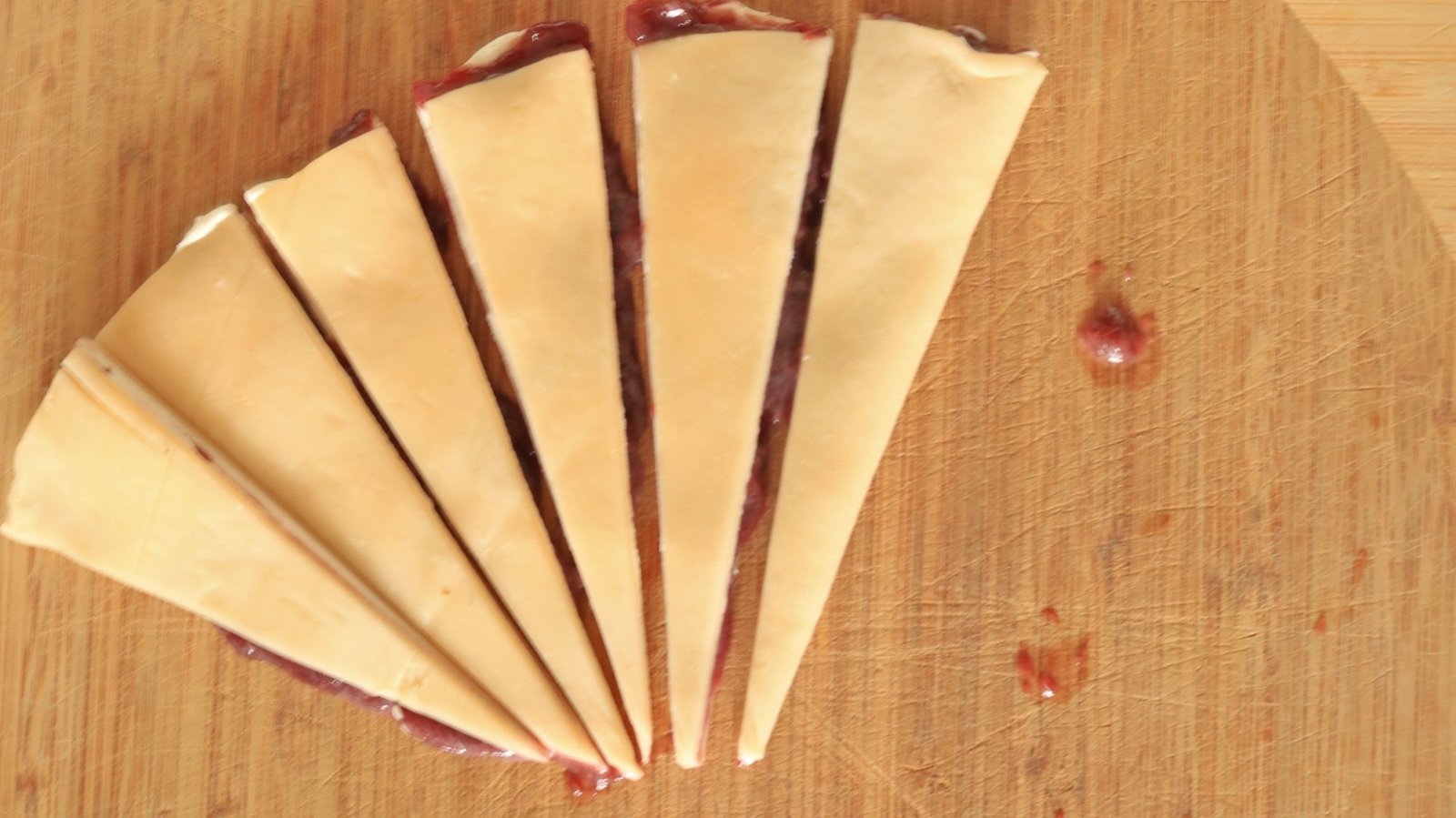 Small wedges of pie crust that have been filled with jam and cream cheese.
