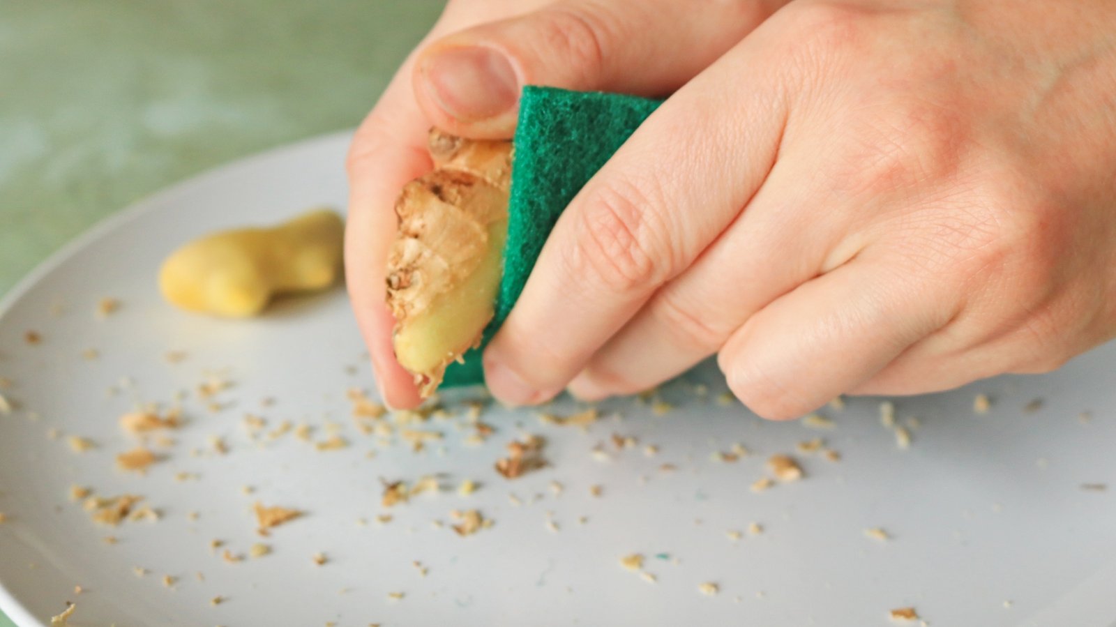 Hand scrubbing ginger root with a green abrasive pad.